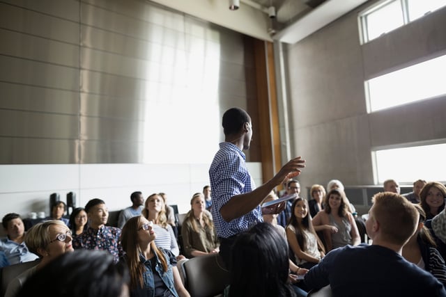 Profesor dando una conferencia entre el público del auditorio.