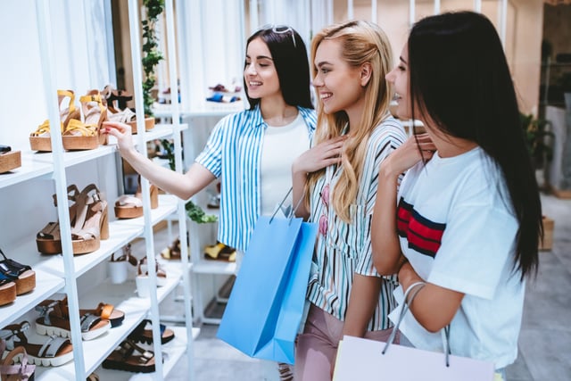 Tres jóvenes haciendo compras en la zapatería en un centro comercial moderno.