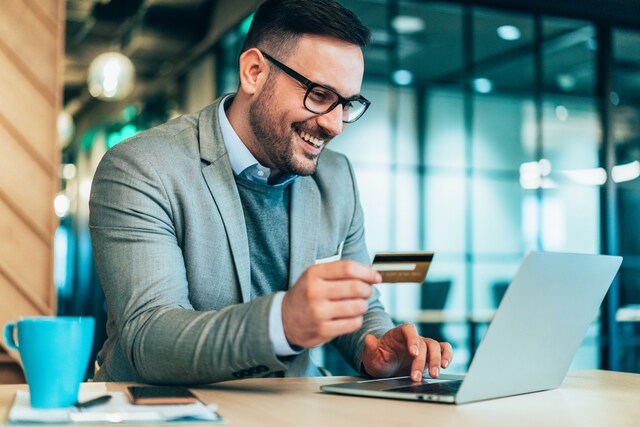 Joven empresario usando tarjeta de corporativa y computadora portátil en una oficina moderna.