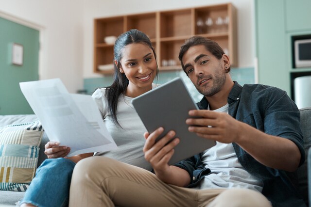 Pareja joven en casa revisando papeles con una tablet.