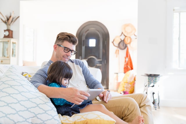 Padre e hija pequeña usando tableta digital en el sofá de la sala de estar.