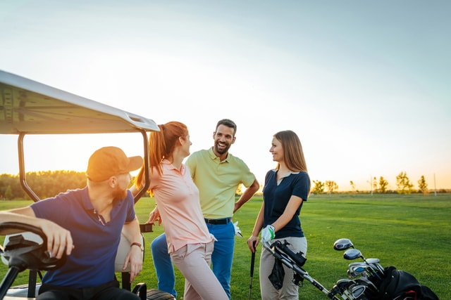 Dos parejas jóvenes platicando en un campo de golf.