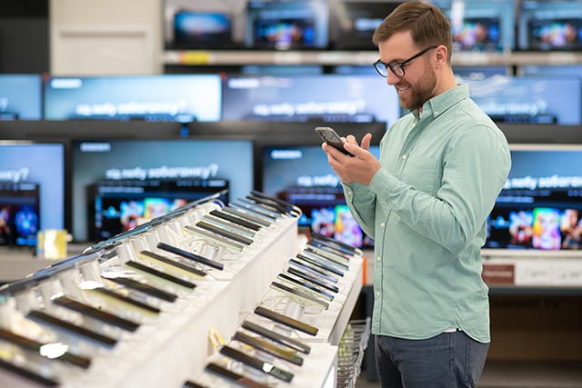 Hombre en una tienda de tecnología revisando un expositor de teléfonos celulares.