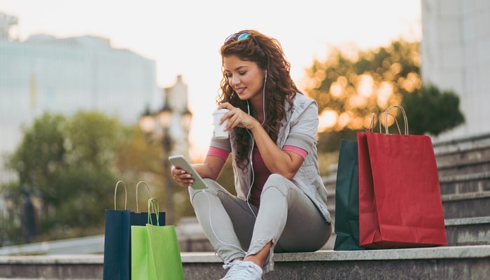 Una mujer descansa durante una tarde de compras, revisando su celular y toma un café.