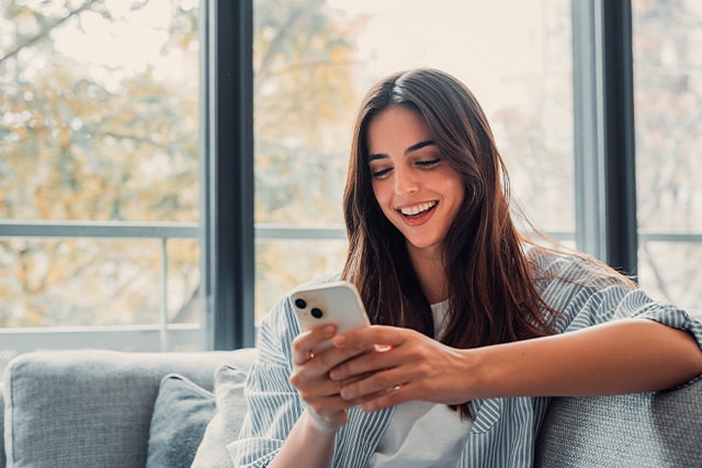 Mujer sentada en casa revisando su celular.