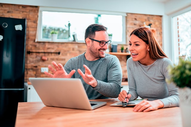 Una pareja sentada a la mesa de la cocina revisando una computadora laptop.