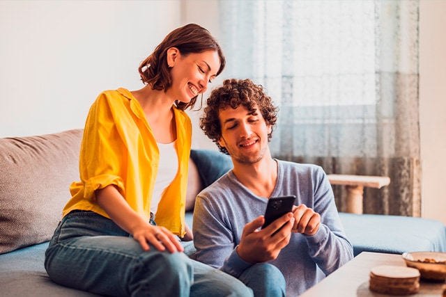 Una pareja en casa revisando información en un teléfono celular.