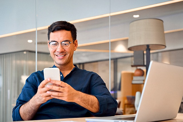 Un hombre en una sala de conferencias después de una reunión, revisando su teléfono celular cerca de una laptop abierta.