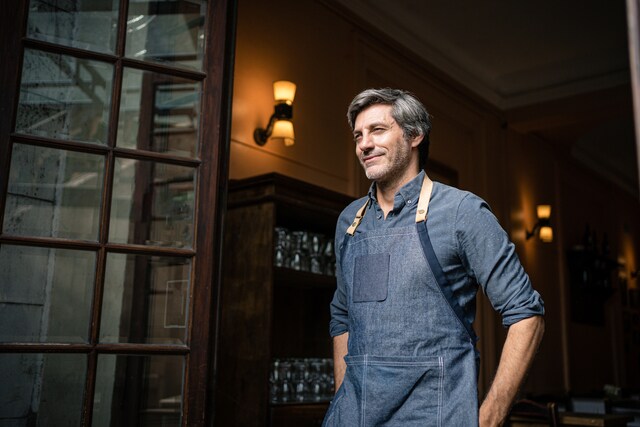 Barista parado en la puerta de un café con un delantal.