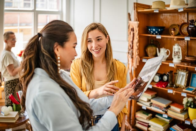 Dos mujeres comentan un artículo vintage en una pintoresca tienda de antigüedades llena de muebles únicos y tesoros retro.