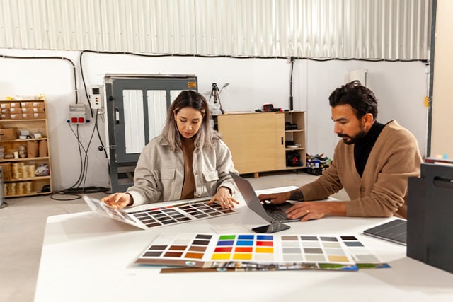 Dos compañeros de trabajo en un taller creativo revisando muestras de color sobre una mesa.