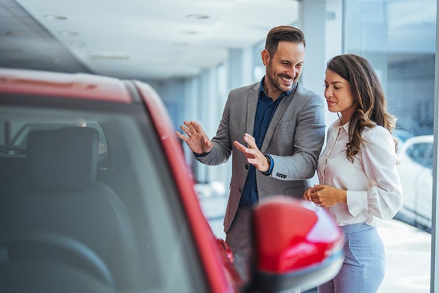 Una mujer habla con un vendedor de autos sobre un vehículo nuevo.