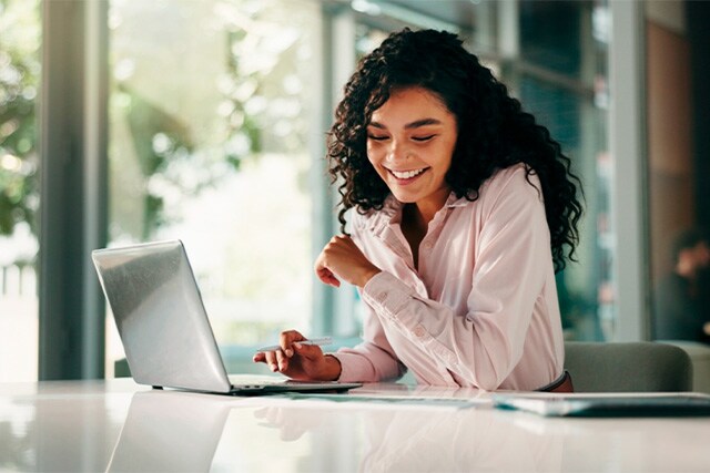 Mujer sonriente sentada en su escritorio trabajando en una laptop.