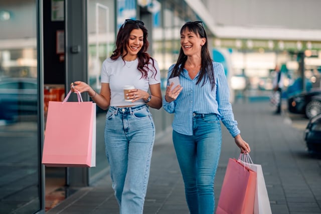 Dos amigas de compras, sosteniendo bolsas de papel.