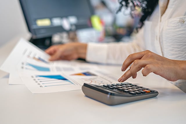 Mujer revisando cifras con algunos gráficos y una calculadora.