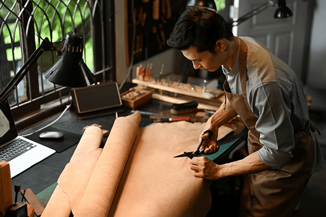 Hombre en su taller cortando un trozo de cuero.