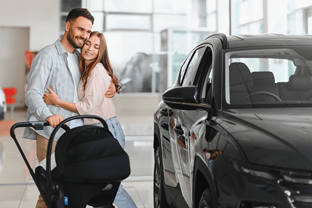 Una pareja con un carriola examina autos nuevos en una agencia de autos.