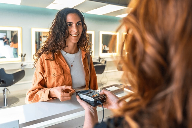 Mujer realizando un pago sin contacto en una peluquería.