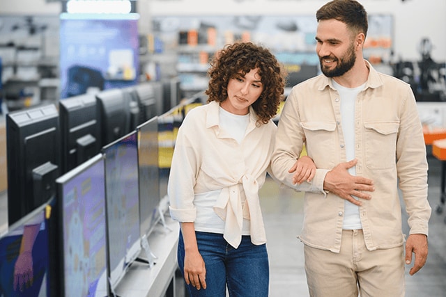 Pareja en una tienda de tecnología revisando televisores nuevos.