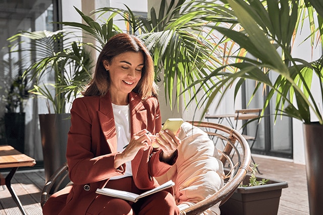 Mujer revisando su teléfono móvil en el vestíbulo soleado de un hotel.