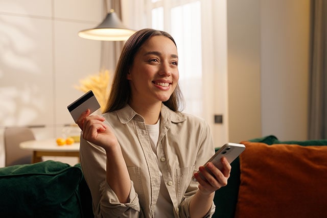 Mujer sosteniendo su teléfono celular y una tarjeta de crédito.