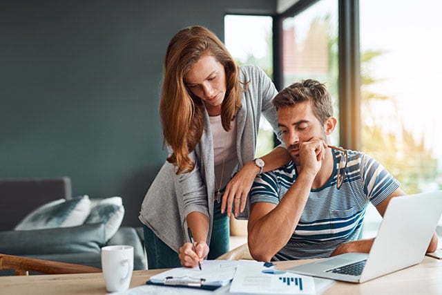 Una pareja en casa revisando documentos financieros en la mesa del comedor.