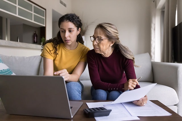 Madre e hija revisan documentos en una computadora portátil en su sala de estar.