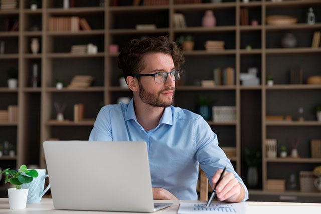 Un hombre en una oficina, tomando notas en una libreta cerca de una computadora portátil.