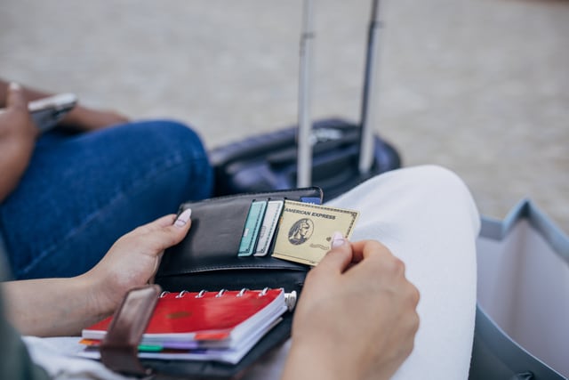 Primer plano de unas manos sosteniendo una billetera y sacando una tarjeta de crédito con artículos personales en el regazo.