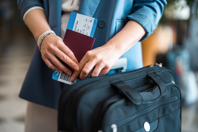 Una empresaria profesional, con un blazer azul, sostiene su pasaporte y su tarjeta de embarque.