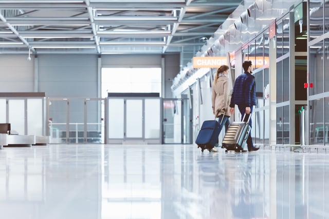Pareja caminando con equipaje dentro de la terminal de un aeropuerto.