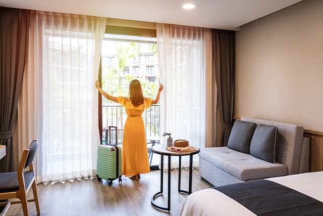 Mujer abriendo las cortinas de su habitación de hotel.