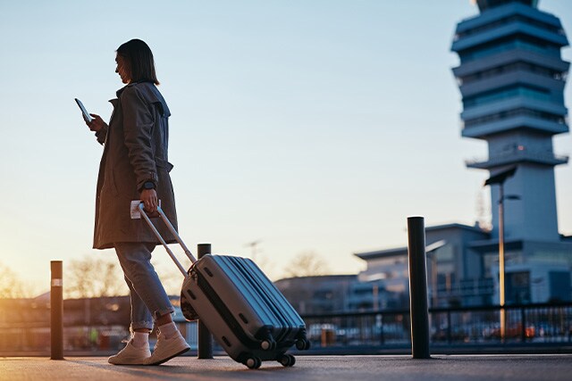 Mujer saliendo de una terminal de aeropuerto con su maleta de mano.