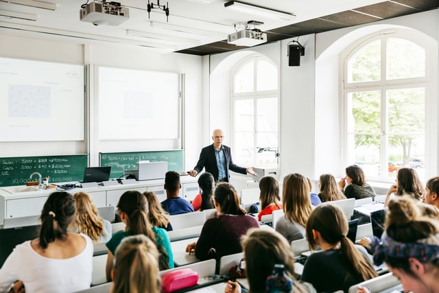 Un profesor universitario se dirige a sus alumnos durante una conferencia en una sala de conferencias moderna y luminosa.