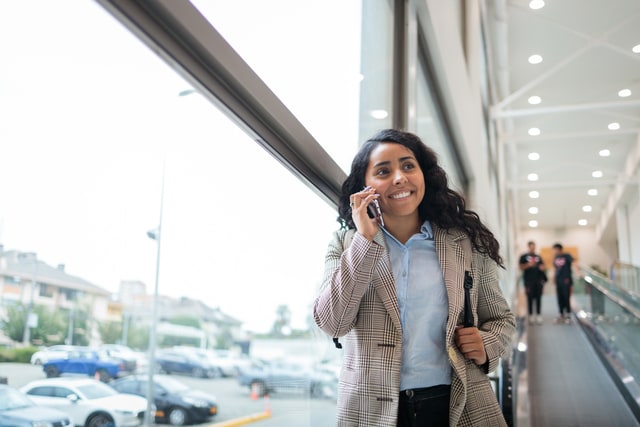 Empresaria usa su celular mientras sube por la pasarela móvil del centro comercial.