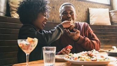 a woman feeding a man a slice of pizza in a restaurant