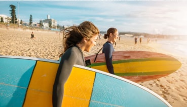 two women carrying surfboards on a sandy beach