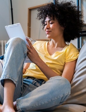 a woman in a yellow shirt is sitting on a couch using a tablet