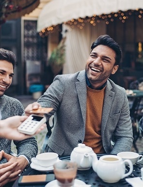 two men are sitting at a table in a restaurant and one of them is holding a credit card .