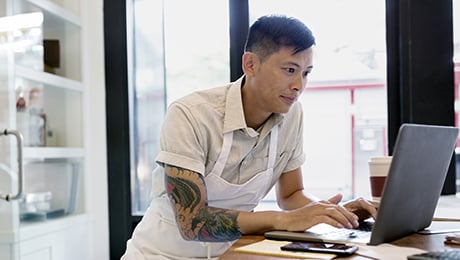 Une personne travaille sur son ordinateur portable, sur un bureau dans son petit commerce.