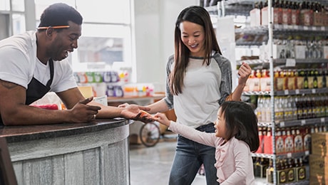 Une personne derrière le comptoire de son petit commerce tend la main à un enfant souriant.
