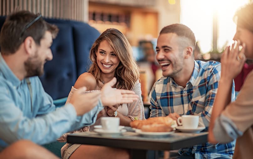 gruppo di amici e amiche scherzano mentre fanno colazione al tavolo di un bar