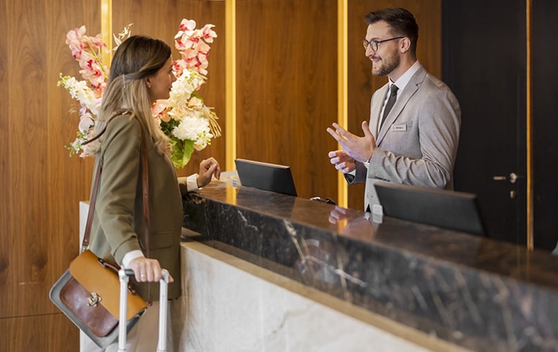 addetto alla reception di un hotel parla con cliente donna     