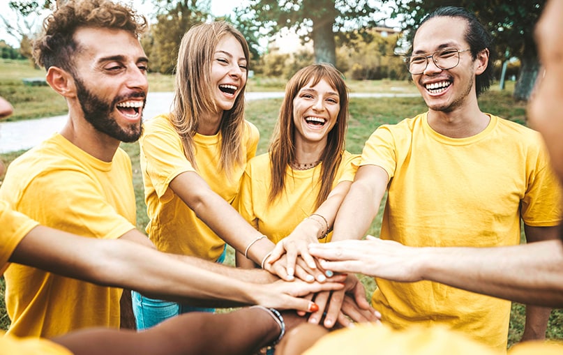gruppo di amiche e amici al parco mettono le mani una sopra l’altra per darsi la carica