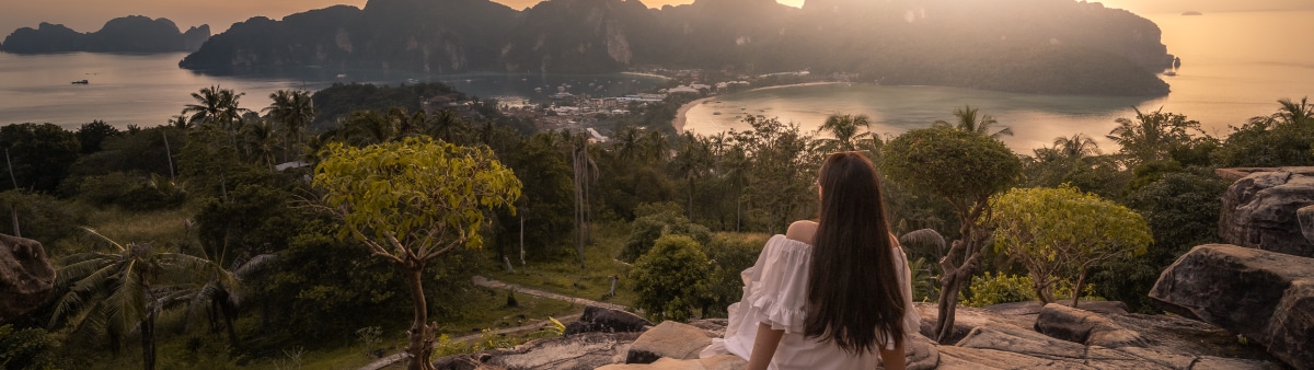 高台の岩場に腰かけて入り江を眺める後姿の女性