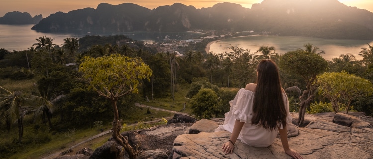 高台の岩場に腰かけて入り江を眺める後姿の女性