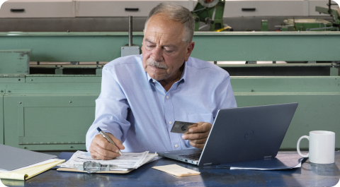 Un comerciante mirando su tarjeta American Express y escribiendo algunas notas en algunos documentos