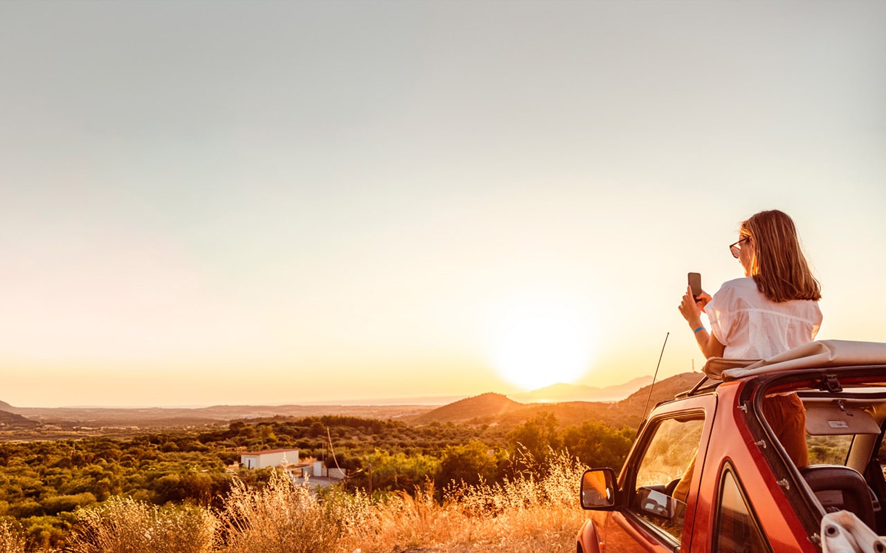 Vanuit haar auto kijkt een vrouw over een grote vlakte naar de zonsondergang