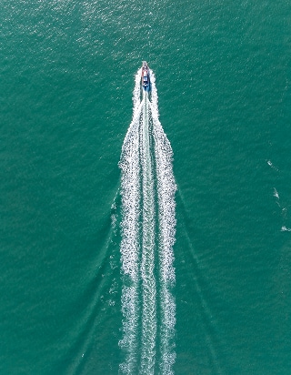 Luchtfoto van een motorboot die op hoge snelheid door groenblauw zeewater vaart en een wit schuimspoor achterlaat.
