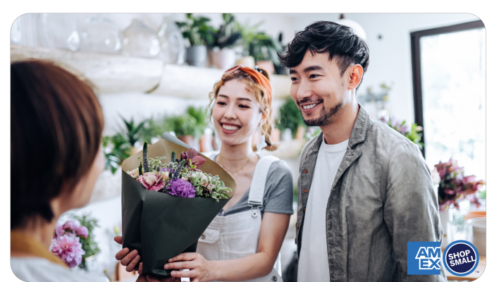 Logo saying “Shop Small with American Express” next to an Asian shoe owner helping a customer find a pair of shoes at a boutique shoe store.